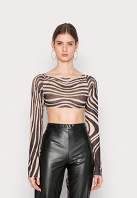 Top cropped de mangas longas feito de um tecido transparente com um padrão de riscas onduladas em bege e preto. Combinado com calças de couro pretas de cintura alta.