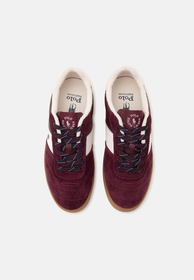 Ζευγάρι μπορντό και λευκά sneakers Polo Ralph Lauren με μαύρα κορδόνια και ταμπά λαστιχένιες σόλες, απεικονιζόμενα από πάνω σε λευκό φόντο.