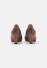 Escarpins en cuir marron avec un bout rond, finition texturée et une hauteur de talon modérée. La vue de derrière montre des lignes fluides et une base robuste.