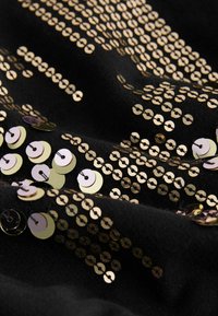 Svart tyg med spridda guld- och metalliska runda paljetter i olika storlekar, vilket skapar ett texturerat, reflekterande ytmönster.