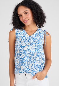 Top senza maniche a fantasia floreale blu con scollatura a V e legacci regolabili sulle spalle. Realizzato in tessuto leggero con una texture liscia.