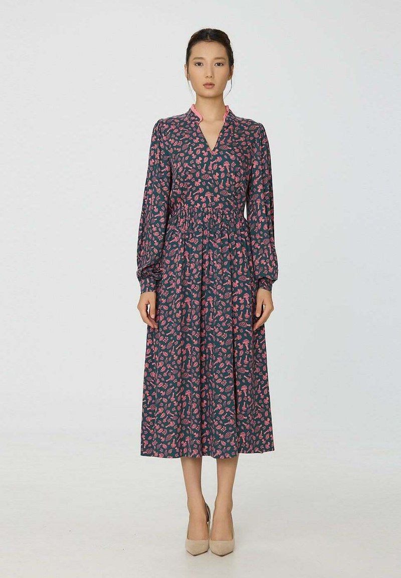 Robe à manches longues en bleu marine foncé avec des motifs floraux roses, col en V, taille froncée et silhouette fluide. Assortie à des talons beiges classiques.