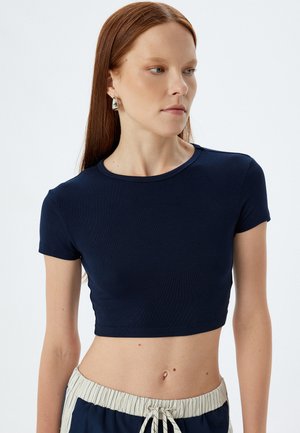 T-shirt cropped bleu marine à manches courtes, fabriqué en tissu côtelé. Design ajusté, encolure ronde, associé à un pantalon avec taille rayée.