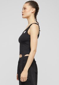 Svart ermeløs crop top laget av bomull, med utskårne detaljer på sidene og en liten logo på brystet for ekstra design.