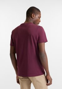 Burgundy short-sleeve t-shirt with a round neck and smooth texture, viewed from the back. Plain design without visible logos or patterns.