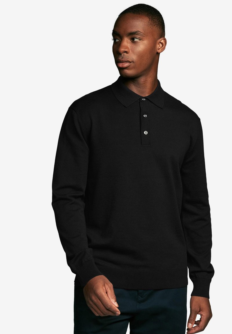 Melna ilga piedurkne polo krekls ar apkakles izgriezumu, trīs pogu aizdari un ribotas aproces, uz vienkārša fona.