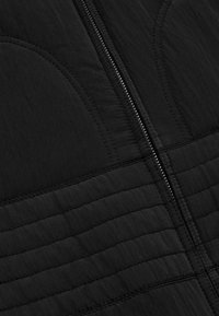 Giacca nera trapuntata con zip centrale, tessuto strutturato con linee verticali e dettagli di cucitura curvi. Materiale leggero.
