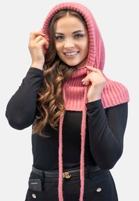 Sciarpa a cappuccio lavorata a maglia rosa con texture a coste, dotata di lunghe fascette, indossata sopra un top nero a maniche lunghe. Tessuto liscio e colore vivace.