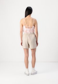 Světle růžový crop top s tenkými ramínky a zavazováním na zádech, doplněný o světle šedé žebrové kraťasy, nošený s bílými vysokými teniskami.