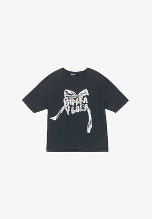 Musta puuvillapaita, jossa on väljä malli ja lyhyet hihat. Paidassa on valkoinen graafinen kuvio, jossa on kaari ja "BIMBA Y LOLA" -teksti.