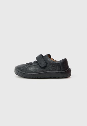 Zapato de cuero negro con superficie texturizada, con una tira de velcro y una suela de goma. Diseño de corte bajo para facilitar el uso.