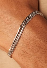 Mooie metalen schakelarmband om een pols, met in elkaar grijpende schakelpatronen, een glanzende zilveren afwerking, een gladde textuur en een klassiek ontwerp.