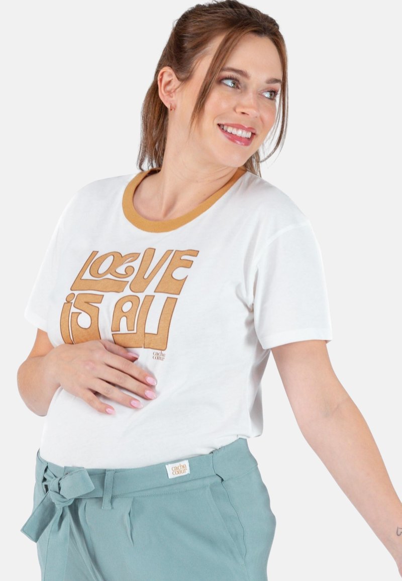 Weißes T-Shirt mit einem runden Senfgelb-Kragen und braunem "LOVE IS ALL" Grafiktext. Kombiniert mit tealten, hochgeschnittenen Hosen mit einer Schleifendetail.