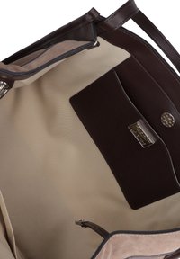 Interno di una borsa a mano in pelle marrone con rivestimento in tessuto beige, caratterizzato da una tasca in pelle scura e hardware con finitura argentata. Dettaglio della chiusura a zip visibile.