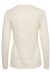 Top in pizzo a maniche lunghe color crema, con motivo floreale e scollatura rotonda. Tessuto liscio con orlo scallopato alle maniche.