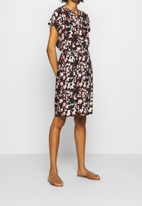 Vestido de manga corta con un estampado floral en rojo, negro y beige, ceñido en la cintura con un lazo a juego. Tejido suave y diseño hasta la rodilla.