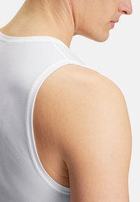 Camicetta bianca senza maniche con una texture a coste, caratterizzata da un colletto rotondo e dettagli di cucitura puliti, mostrata da dietro con una spalla liscia.