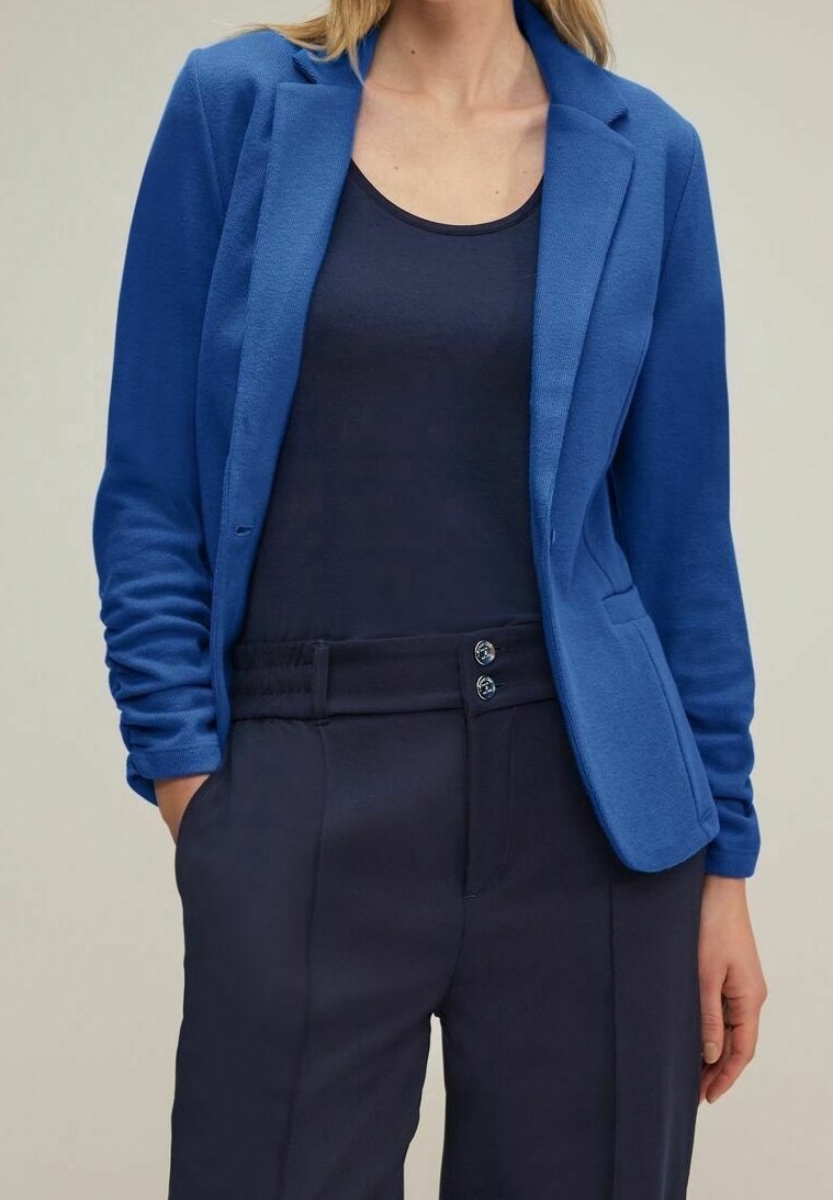 Blå kavaj i strukturerad tyg, med en knappstängning och två framfickor, bärs över en marinblå tank-top och skräddarsydda byxor.