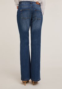 Vaqueros acampanados de color azul con una cintura de altura media, que cuentan con dos bolsillos traseros y un lavado claro. El dobladillo está ligeramente deshilachado, realzando el estilo casual.