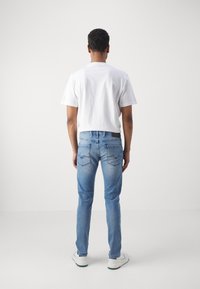 Ljust blå denimjeans med en tajt passform, som har två bakfickor med zickzack-sömnad, bärs med en enkel vit t-shirt och vita sneakers.