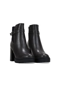 Botas de cuero negro hasta el tobillo con un alto tacón cuadrado, cremallera lateral y detalle de correa ajustable en el tobillo. Suela de goma texturizada para mayor agarre.