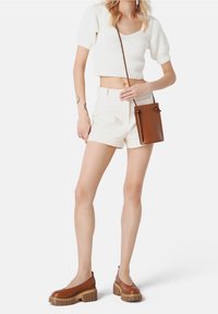 Hnědé kožené boty s robustními podešvemi, bílé pletené crop top a světle béžové šortky. Hnědá crossbody taška s detailem stáhnutí.