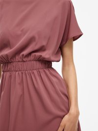 Bordo zbrana obleka s kratkimi rokavi, elastičnim pasom in mehko, tekočo tkanino, ki prikazuje minimalno teksturo in padajočnost.