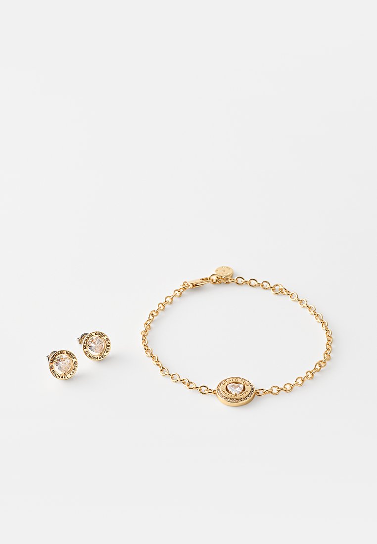 Conjunto de joyería en tono dorado que incluye pendientes de aro con cristales claros y una pulsera a juego con un medallón central decorado.