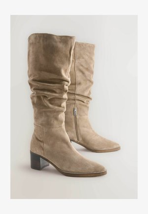 Bež usnjeni škornji do kolen z zloženim dizajnom, koničastim nosom in lesenim blokastim petnikom. Imajo stransko zadrgo za enostavno obuvanje.