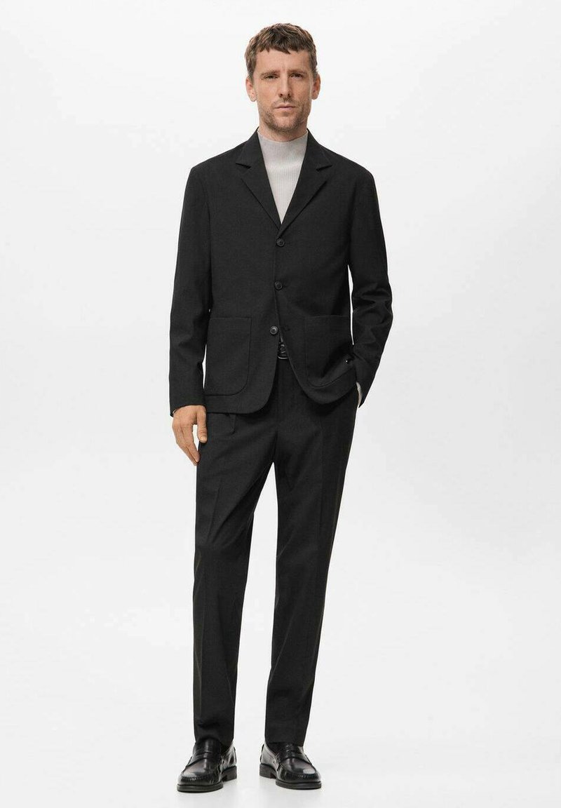 Completo nero realizzato in tessuto testurizzato con una vestibilità su misura, caratterizzato da un blazer a un bottone e pantaloni dritti, abbinato a un collo alto leggero.