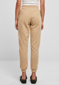 Beige joggebukser med tapered ben design, elastisk linning, mansjetterte hem og en myk, glatt tekstur. Brukt med svarte platåsandaler.