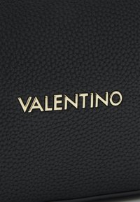 Sac en cuir noir texturé avec un logo "VALENTINO" en or bien en vue. Design compact avec une finition lisse et des détails raffinés.