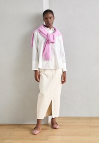 Vit skjorta, krämfärgad midikjol med sprund fram, och en ljusrosa tröja över axlarna. Rosa flats med dekorationer.