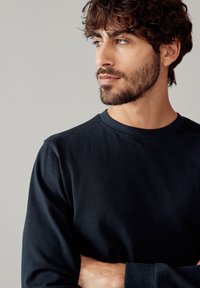 Maglietta a maniche lunghe di colore blu navy con scollatura rotonda, realizzata in tessuto morbido, con una silhouette aderente e un design minimalista.