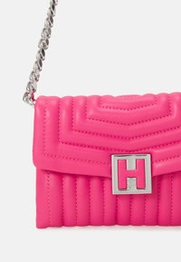 Vaaleanpunainen tilkkutyylinen nahkalaukku, jossa on hopeinen ketjun olkahihna, ja jossa on näyttävä hopeinen "H"-solki sekä pystysuuntainen ompelutaja.