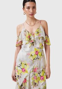Bloemjurk met cold-shoulder ontwerp. Gemaakt van lichte stof, met roze en groene orchideeën patronen, een V-halslijn en ruches accenten.