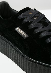 Baskets plateforme Puma noires avec semelle épaisse texturée, lacets noirs et logo Puma doré sur tige en daim.