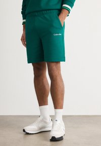 Grønne atletiske shorts med elastisk waistband og sidelommer. Har et lille hvidt "Calvin Klein" logo på venstre lår.