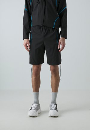 Schwarze Shorts mit einem Kordelzugbund, versehen mit blauen Akzenten und seitlichen Taschen, kombiniert mit grau-weißen Sneakers und hellgrauen Socken.