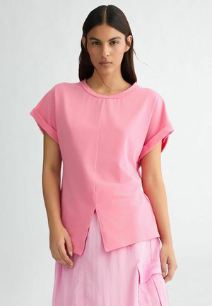 Top rosa chiaro a maniche corte con scollo rotondo e dettaglio spacco frontale. Realizzato in tessuto morbido con una texture liscia.