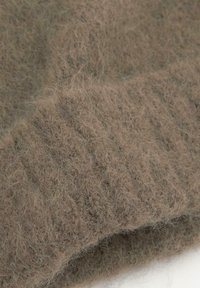 Brun strikket sweaterdetalje, der viser en blød, fuzzy tekstur med et subtilt mønster og ribbede detaljer.