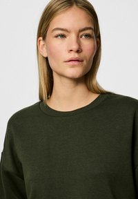 Felpa verde scuro con scollo a girocollo, caratterizzata da una texture liscia e una vestibilità comoda. Nessun motivo visibile o dettagli in metallo.