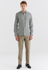 Czarna i biała koszula w groszki z długimi rękawami, zestawiona z beżowymi spodniami i czarnymi butami, na neutralnym tle.