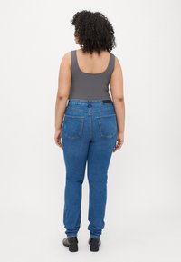 Siv bodi z kvadratnim hrbtom, v kombinaciji z modrimi ozkimi jeans hlačami z zmerno visokim pasom in dvema zadnjima žepoma. Črne pete.