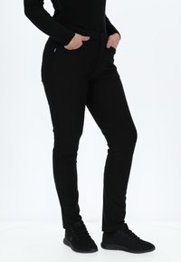 Zwarte stretchbroek met een slim fit, voorzien van twee zijzakken, een gladde tailleband en gecombineerd met zwarte sportschoenen.