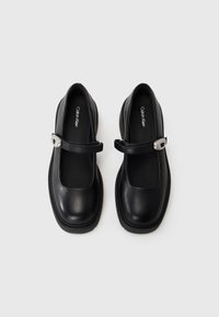 Scarpe Mary Jane in pelle nera con punta rotonda, dotate di una fascia con una fibbia argentata e una suola in gomma texturizzata bassa.