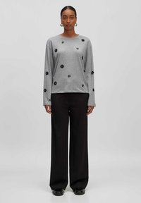 Grijze sweatshirt met lange mouwen en zwarte bloemenapplicaties, gecombineerd met brede zwarte broeken en zwarte schoenen, wat een casual outfit creëert.