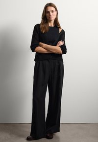 Suéter de punto negro con un corte holgado y mangas anchas, combinado con pantalones negros de cintura alta. Textura suave y color sólido, detalles mínimos.