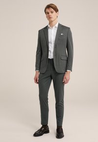 Grå skräddarsydd kostym med smala byxor, texturerad tyg och en näsduk i fickan. Bärs över en vit skjorta och kompletteras med mörka loafers.