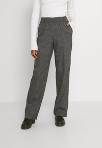 Pantalons à carreaux gris avec une coupe décontractée, taille élastique et poches latérales, associés à un haut à manches longues côtelé blanc et des chaussures noires.